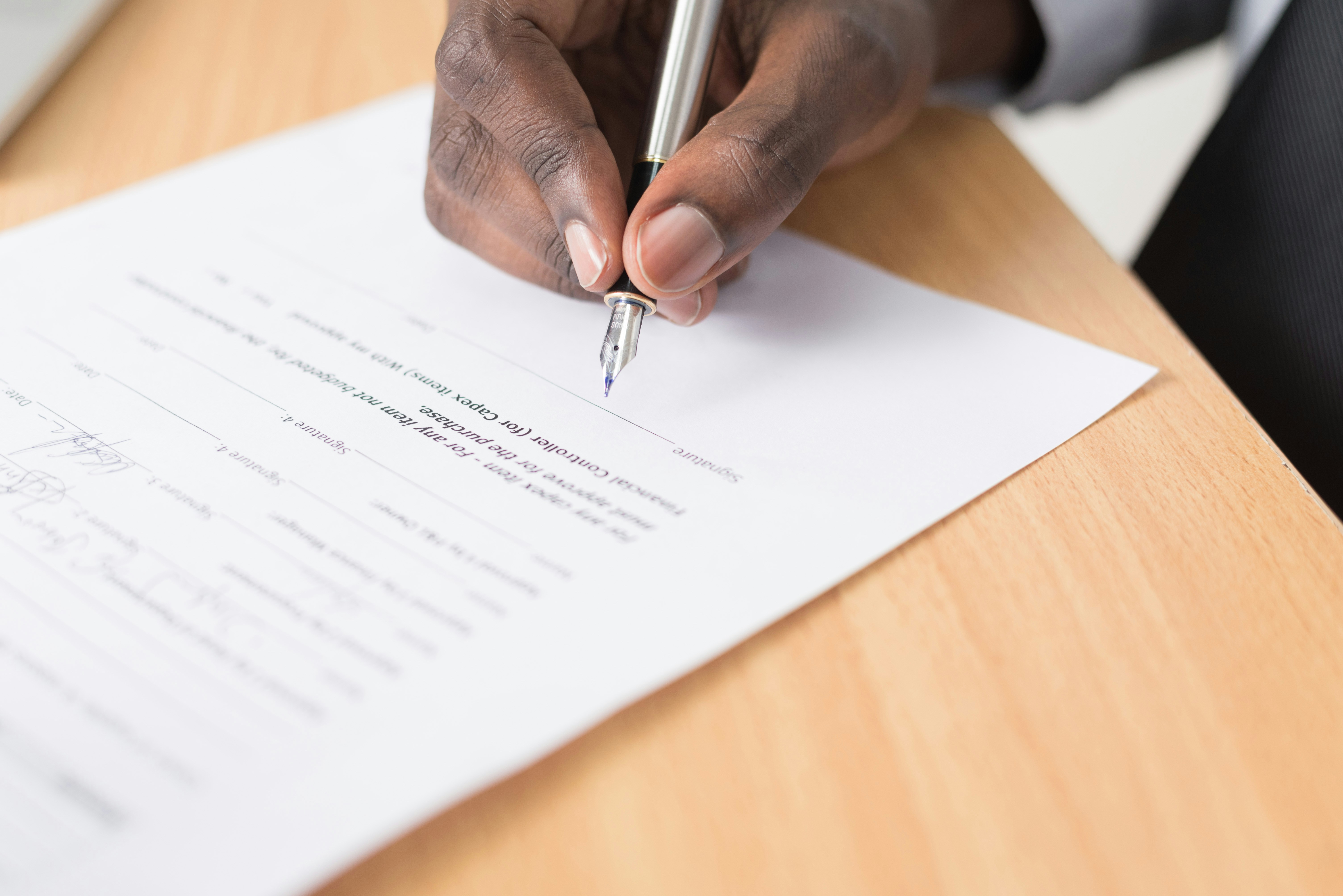 A Black person holds a pen and writes on a contract. 