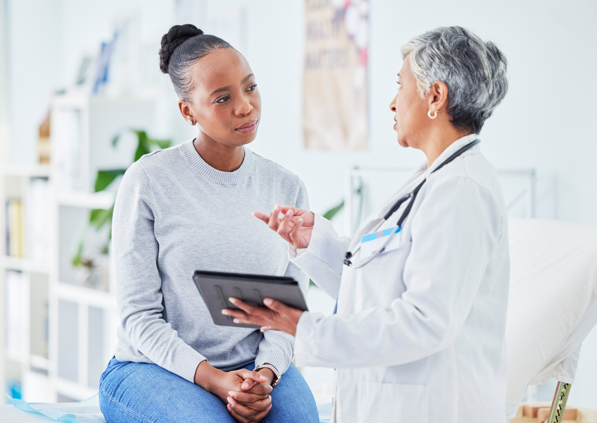 A Black femme patient listens to an older Black woman doctor. 
