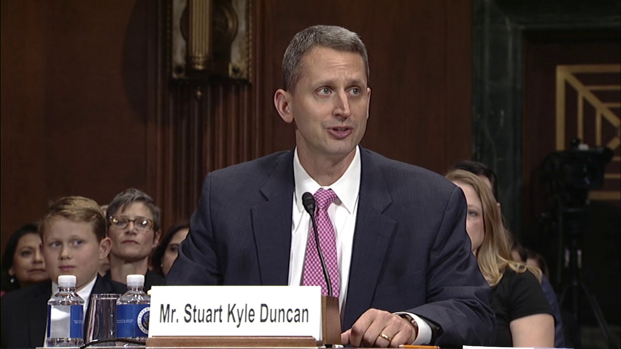 Kyle Duncan testifying at a hearing before the Senate Judiciary Committee. He is speaking, and there are several people in the background.