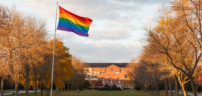 A rainbow flag flies outside of a school building (Photo Credit: Megan Long Photography)
