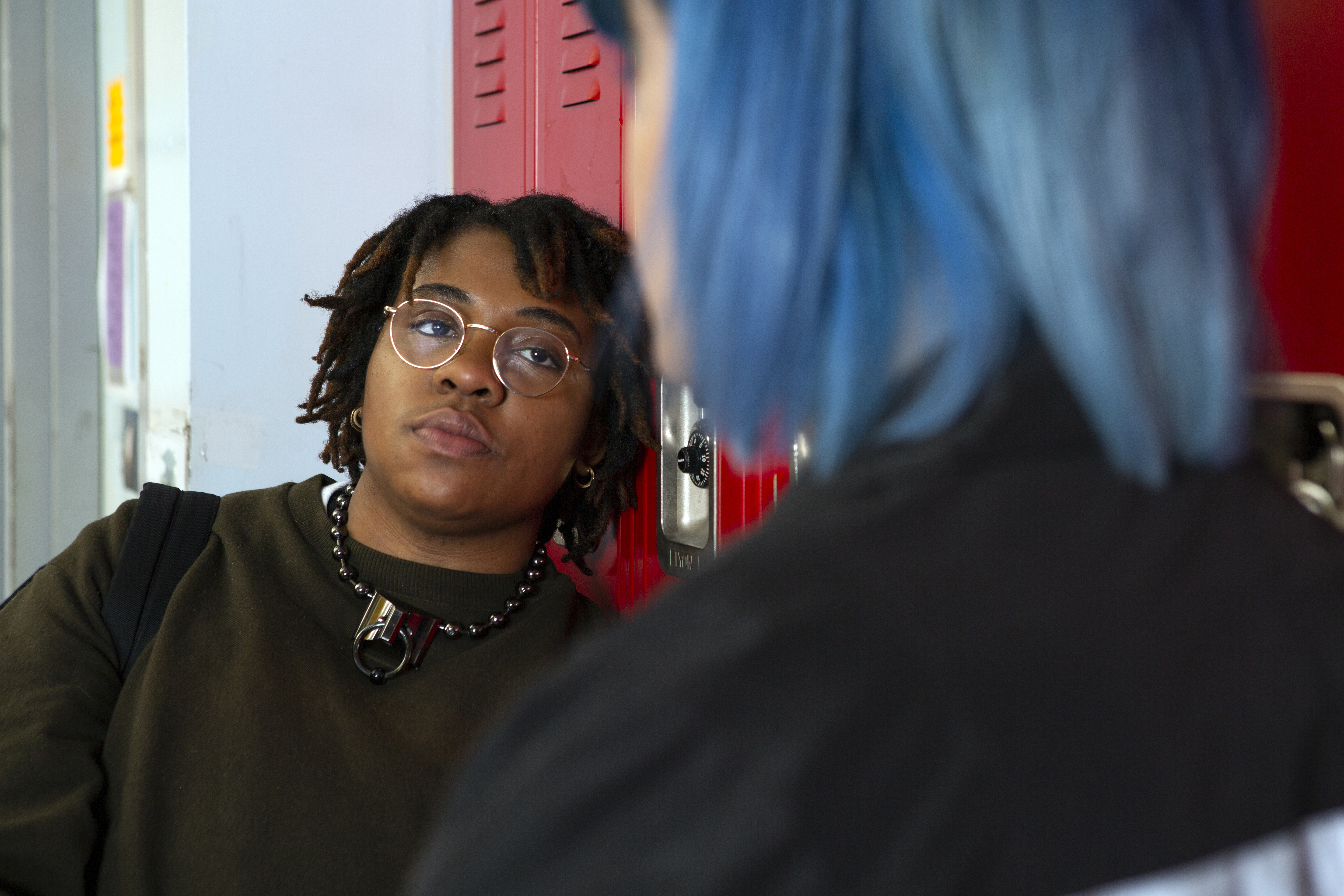 A non-binary student talking to a friend in front of their locker