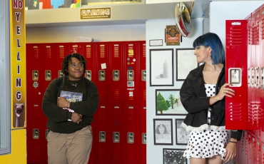 Two non-binary students looking at eachother in a school hallway