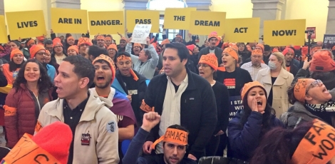 A crowd of protesters, many wearing orange hats and headbands, in the rotunda of the U.S. Capitol. Protesters in the back hold up signs saying "Our lives are in danger. Pass the Dream Act now!"