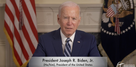 President Biden sitting at desk with digital banner showing he/him pronouns